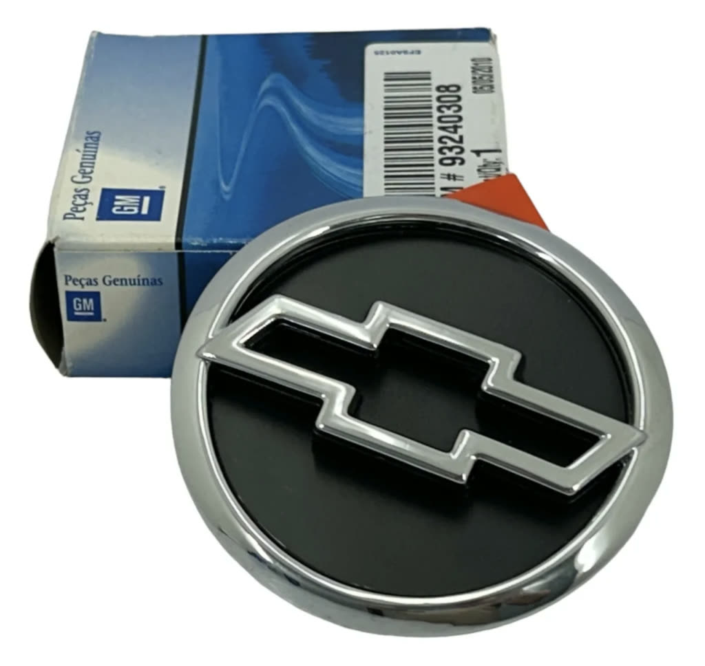 Emblema de grade dianteira GM cromado com a gravata Chevrolet, ao lado da caixa de peça genuína GM